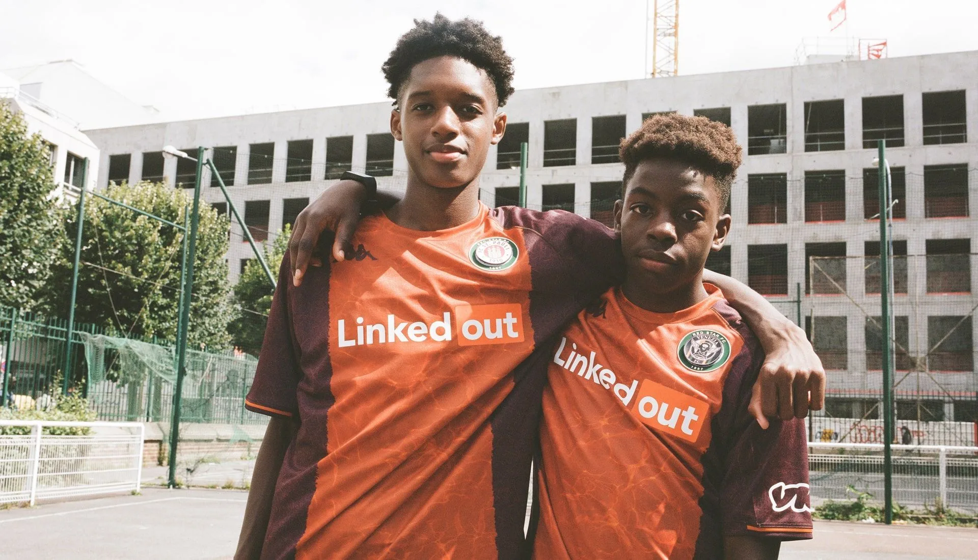 Two young players wearing matching Red Star Paris orange away jerseys at a city pitch